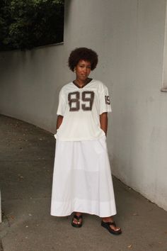 a woman standing in front of a wall wearing a white shirt and skirt with the number 89 on it