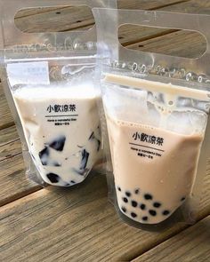 two bags of bubble tea sitting on top of a wooden table next to each other