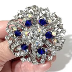 "Something blue bridal brooch with sapphire blue accent featuring flower or floral round shape made of sparkly clear mixed with AB iridescent colored rhinestone crystals in tarnish-resistant silver rhodium plated base.   Brooch measures about 2 1/8\" (5.5cm) in diameter. Note: AB (Aurora Borealis) crystal has an iridescent coating that gives it a subtle shimmer which takes on the colors around it. * Limited, only a few left now View all something blue designs at https://etsy.me/1aLVWtA View all Blue Brooch For Wedding Jewelry, Blue Wedding Brooch Jewelry, Wedding Brooches With Rhinestones, Luxury Sapphire Wedding Brooches, Elegant Blue Wedding Brooches, Elegant Blue Jeweled Brooches, Blue Flower Brooch For Wedding, Crystal Flower Brooch For Weddings, Ornate Blue Wedding Brooches