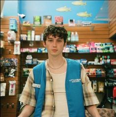 a young man standing in front of a store filled with items and looking at the camera