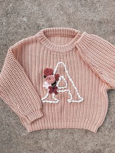 a pink knitted sweater with flowers on the front and back, sitting on concrete