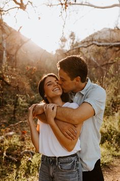 a man and woman embracing each other in the woods at sunset with sunlight shining on them