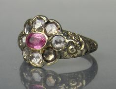 "Well this is just one of those rarities that doesn't come along very often! A later Georgian foil-backed natural pink sapphire and rose cut diamond ring with a floral band circa 1820. This ring originally had black enamel in the recessed areas of the band with traces of it still visible today. The rose cuts are very sparkly but with a dark sparkle, several of these stones would be considered fancy-color light brown (this is not due to the foil color, but the color of the diamond). There is no m Pink Hallmarked Victorian Ruby Ring, Victorian Pink Hallmarked Ruby Ring, Pink Victorian Hallmarked Ruby Ring, Victorian Style Pink Ruby Ring Gift, Victorian Ruby Ring With Single Cut Diamonds, Antique Pink Ruby Ring, Antique Pink Ruby Ring With Rose Cut Diamonds, Antique Pink Rings With Center Stone, Antique Pink Rose Cut Diamond Jewelry