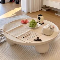 a white table topped with a bowl of grapes next to a toaster and book