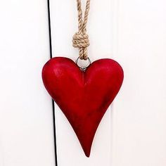 a red heart hanging from a rope attached to a white door with a knot around it