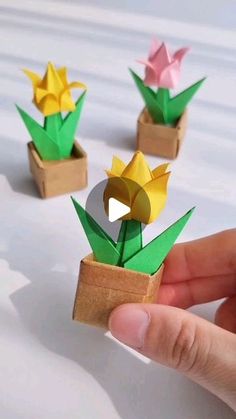 origami flowers in small wooden boxes on white tablecloth with hand holding one