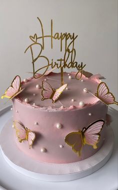 a birthday cake with pink frosting and gold butterflies on top, sitting on a plate