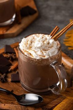 there is a cup of hot chocolate with whipped cream and cinnamon sticks on the side