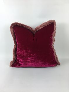 a red velvet pillow with fringe edges on a white background