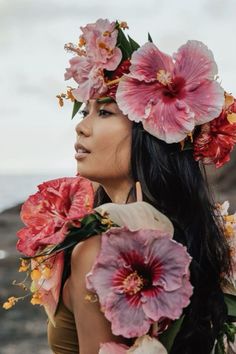 a woman with flowers in her hair standing near the ocean and looking off into the distance