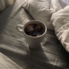 a cup of tea sitting on top of a bed covered in white sheets and pillows