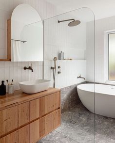 a white bath tub sitting next to a bathroom sink under a large mirror on top of a wooden cabinet