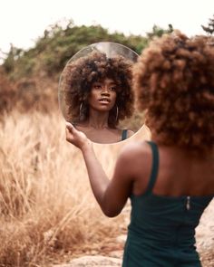 a woman is looking at her reflection in the mirror while she brushes her afro hair