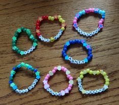 four bracelets with name beads on them sitting on a wooden table next to a cell phone