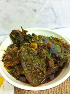 a white bowl filled with meat and greens on top of a table next to a banana