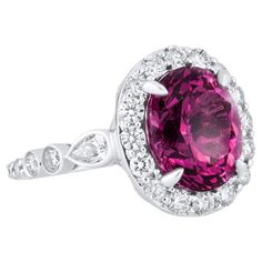 Behold, a ring that's bound to steal your heart and captivate the eyes of all who gaze upon it. This stunning masterpiece is a true testament to the beauty that can be found in the world of fine jewelry. At its heart lies a vibrant 6.04-carat oval cut Raspberry Garnet, a gemstone that embodies passion, vitality, and love. Its deep, rich hue is as unique as it is mesmerizing, making it the perfect symbol of individuality and creativity. The Raspberry Garnet takes center stage, embraced by a delic Dazzling Oval Gia Certified Rings, Gia Certified Oval Platinum Ring, Oval Cluster Ring With Gemstone In Platinum, Oval Platinum Cluster Ring With Gemstone, Platinum Oval Halo Ring With Gemstone, Oval Platinum Halo Ring With Gemstone, Dazzling Oval Ruby Ring With Halo Setting, Gia Certified Oval White Gold Ring, Oval Ruby Ring In White Gold With Halo Design