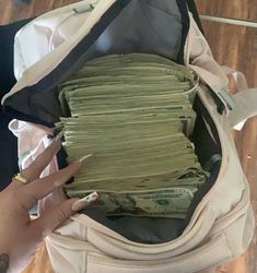 a woman's hand is on top of stacks of money in an open suitcase