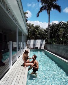 a man and woman are sitting in the water next to a swimming pool with palm trees