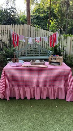 a red and white checkered table cloth on top of a wooden bench in front of a fence