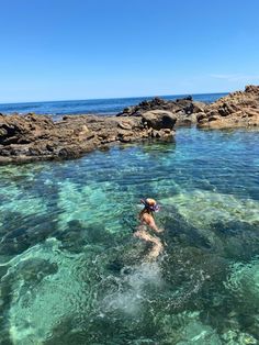 a person swimming in clear blue water next to rocks and the ocean on a sunny day