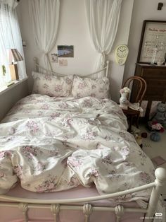 a white bed with pink flowers on it in a bedroom next to a dresser and window