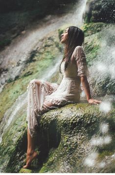 a woman sitting on top of a rock next to a waterfall