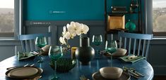 a dining room table set for four with blue walls and white flowers in vases