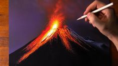 a person is holding a pencil and drawing a volcano with bright red, orange and yellow lights