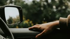 a person's hand on the steering wheel of a car with trees in the background