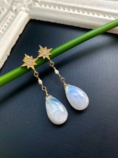 Introducing our handmade rainbow Moonstone and freshwater Pearl 14K gold filled gold star stud dangle earrings! These enchanting earrings are the perfect addition to any jewelry collection.The earrings are delicately crafted with high quality 14K gold filled wire, which is sturdy and long lasting, but also lightweight and comfortable to wear. The studs are made of 14K gold plated brass and feature a star shaped design that gives them a celestial and astral appeal. Each earring is encrusted with Celestial Gemstone Drop Earrings, Celestial Dangle Earrings For Anniversary, White Star-shaped Earrings For Wedding, White Celestial Star Earrings, Celestial White Star Earrings, White Star-shaped Wedding Earrings, Star-shaped Pearl Drop Jewelry As Gift, Star-shaped Pearl Drop Jewelry For Gifts, Celestial Teardrop Earrings For Gift