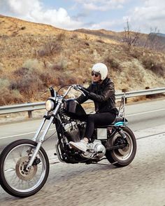 a man riding on the back of a motorcycle down a road next to a hillside