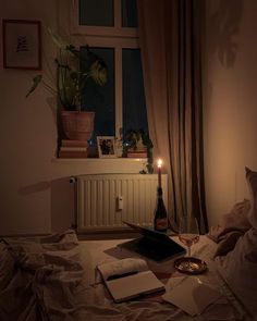 a bottle of wine sitting on top of a bed next to an open book and candle