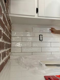 a person is painting a brick wall in a kitchen with white cabinets and counter tops