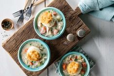 three bowls of chicken pot pie soup on a wooden board with silverware and utensils