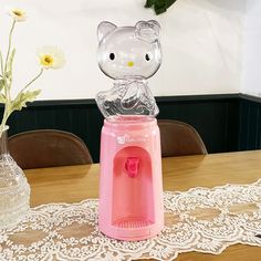 a hello kitty water dispenser sitting on top of a table next to a vase with flowers