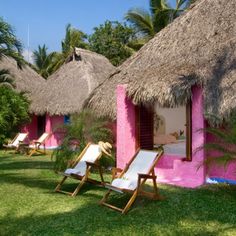 several lawn chairs and thatched huts in the grass with palm trees on either side