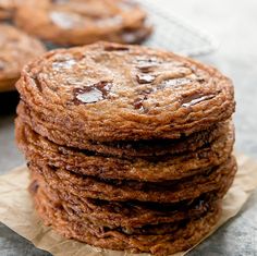 a stack of chocolate chip cookies sitting on top of a piece of wax paper next to a cooling rack