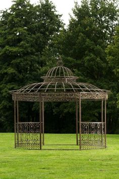 a metal gazebo in the middle of a grassy field with trees in the background