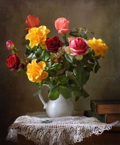 a white vase filled with lots of colorful flowers on top of a table next to two books