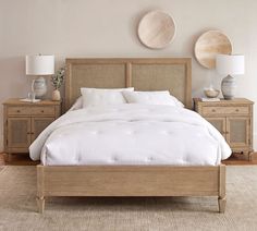 a bed with white sheets and pillows in a bedroom next to two wooden nightstands