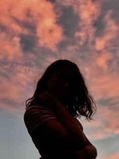 a woman standing in front of a pink and blue sky with clouds above her head