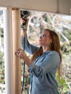 a woman is working on the side of a house with a power drill in her hand