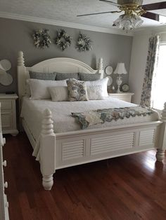 a white bed sitting on top of a hard wood floor next to a wall mounted fan