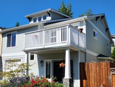 a house with white balconies and flowers in the front yard on a sunny day