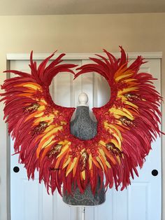 a red and yellow feathered wreath on a mannequin's head in front of a white door