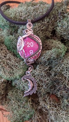 a necklace with a pink pendant hanging from it's side on top of some moss