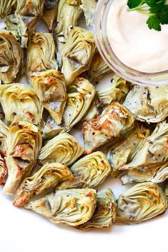 artichokes with sauce and garnish on a white plate next to a small bowl