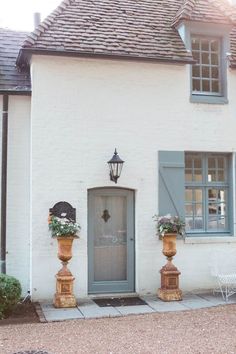 a white house with blue shutters and potted plants on the front door is shown