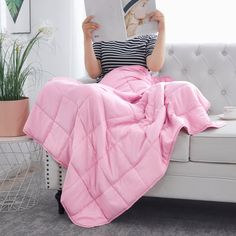 a woman is sitting on a couch reading a book and holding a magazine in her hands