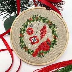 a cross stitch christmas ornament hanging from a red ribbon next to a tree